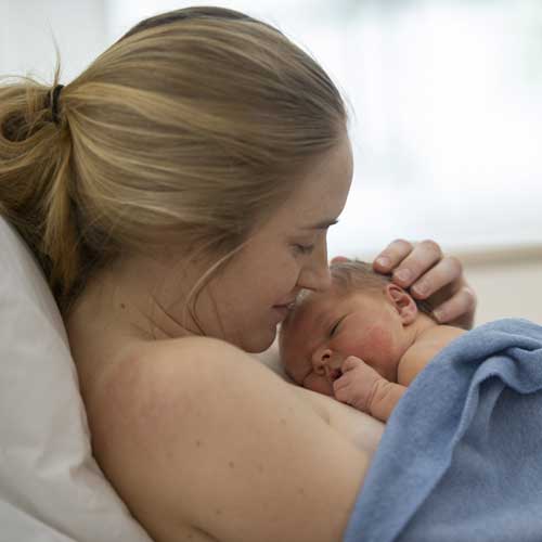 A mother and her baby doing skin-to-skin at the hospital under a blanket.