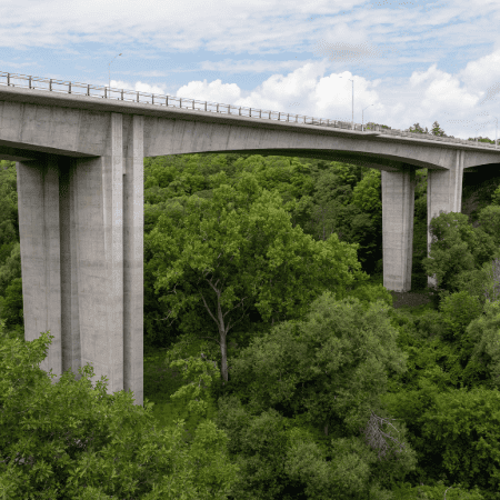 A side view of a large bridge spanning a densely wooded ravine.