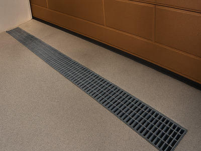 A drain grate in front of a garage door.