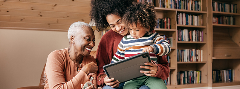 image of three generation family sitting with tablet and laughing together