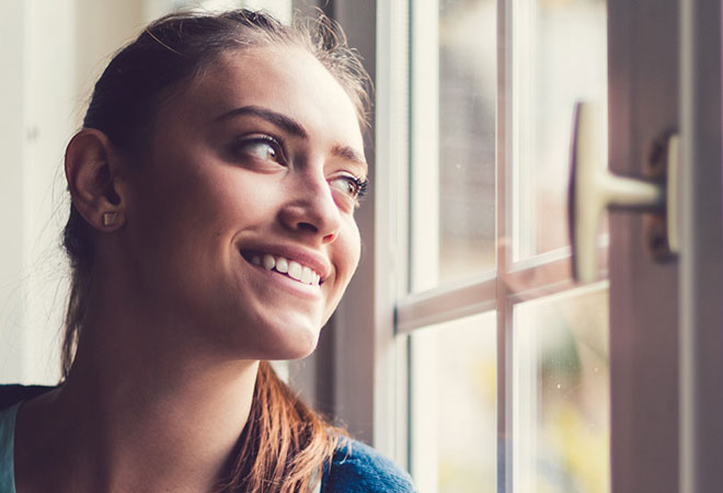 young woman looking out a window smiling