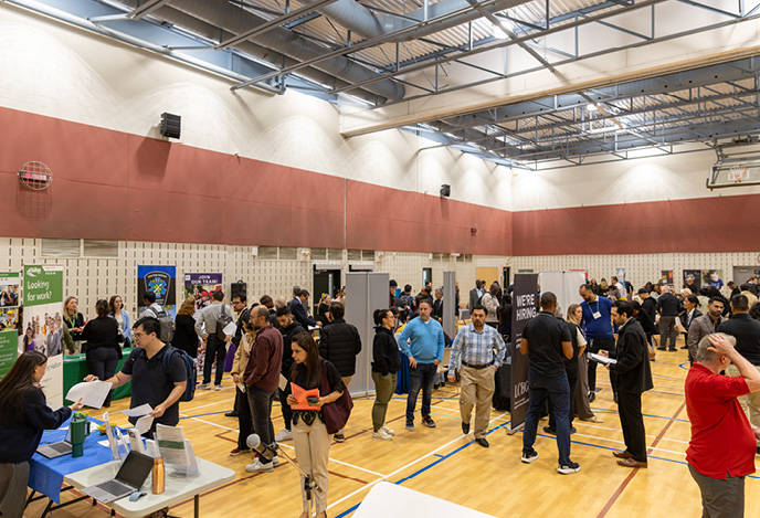Crowd of people at the job fair in the gymnasium at Halton Regional Centre, with multiple booths and attendees engaging with employers.
