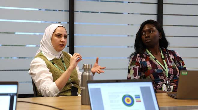 Woman presenting in a meeting room while another listens.