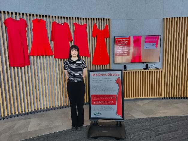 A woman stands near a display of several bright red dresses of different shapes and sizes.