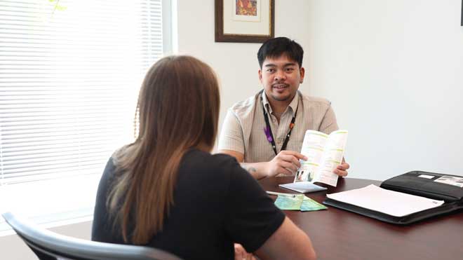 Man holding a pamphlet open and pointing out a service listed within to a person with long hair