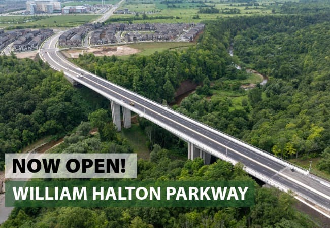 An aerial view of a bridge over a heavily wooded ravine with the text 'now open: William Halton Parkway.'