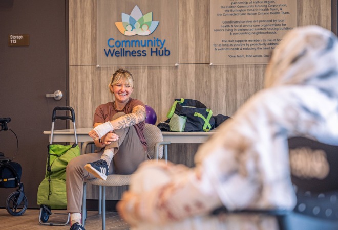 A smiling woman sitting in front of a sign that says "Community Wellness Hub".