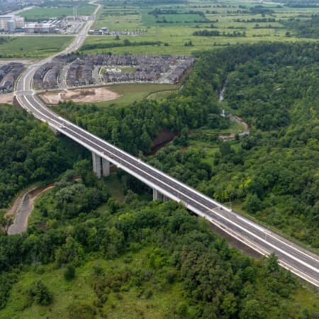 Aerial photo of a new 4-lane bridge over a densely wooded creek.