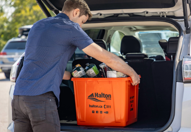Person placing a orange bin into the back of his automobile